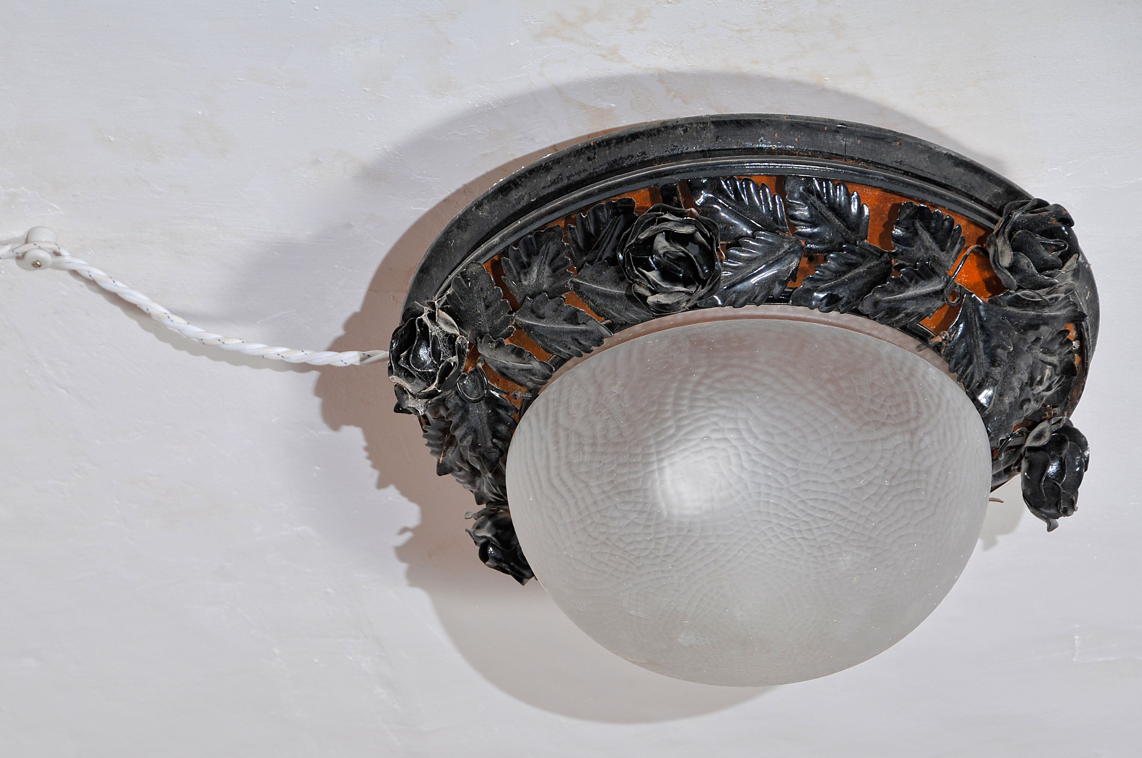 Eine Wandleuchte mit einer gläsernen, strukturierten Schirm und aufwendiger Metallverzierung.