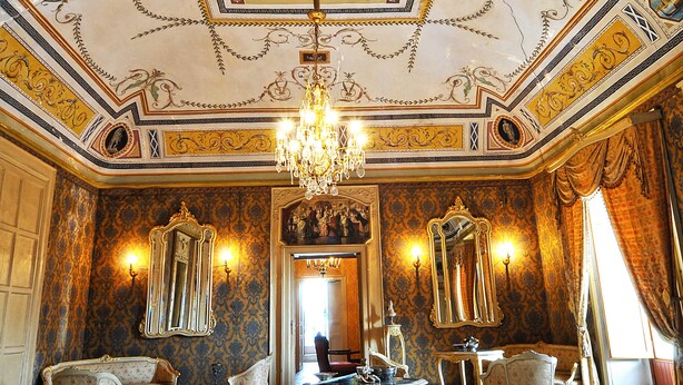 Una sala imponente con techo ricamente decorado, candelabros y muebles clásicos.