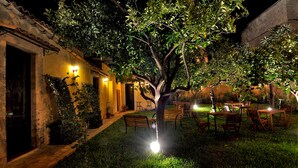 Un patio con un árbol, asientos al aire libre y un edificio con techo de tejas.
