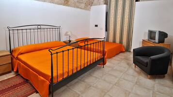 A bedroom with a metal bed frame, orange bedding, a wooden nightstand, a television on a wooden cabinet, and a patterned rug.