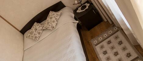 A neatly made bed with a patterned bedspread and pillows, a small bedside table with a lamp, and a rug on a wooden floor.