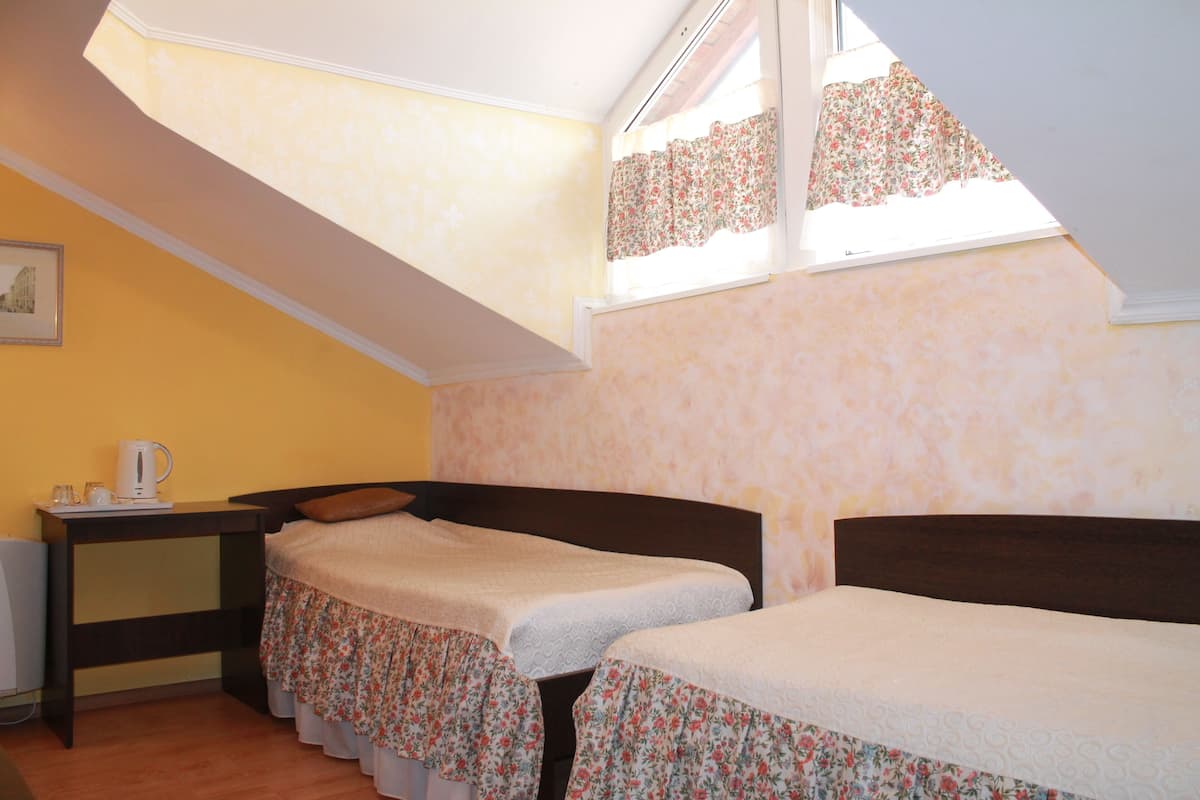Une chambre avec deux lits, une petite table avec une bouilloire et une fenêtre ornée de rideaux à motifs floraux.