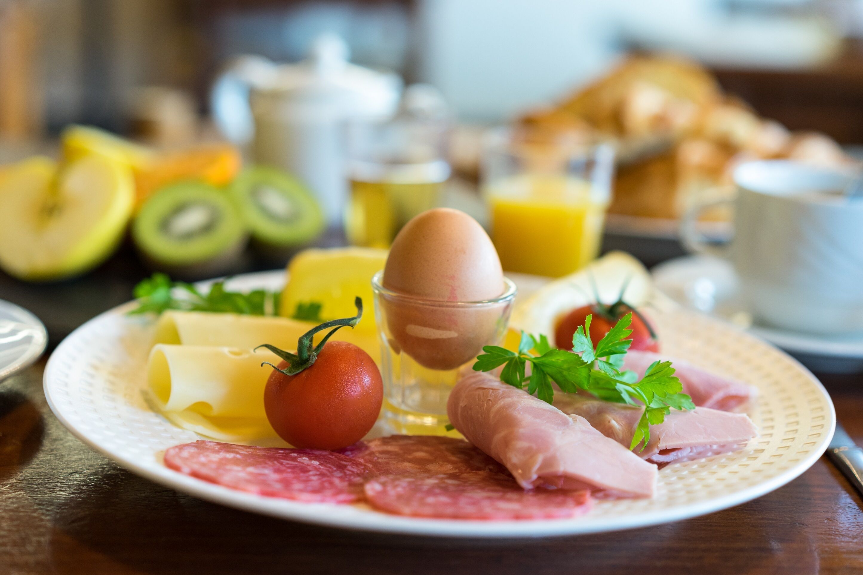Une assiette de petit-déjeuner comprenant des œufs, du fromage, des tomates et de la charcuterie.