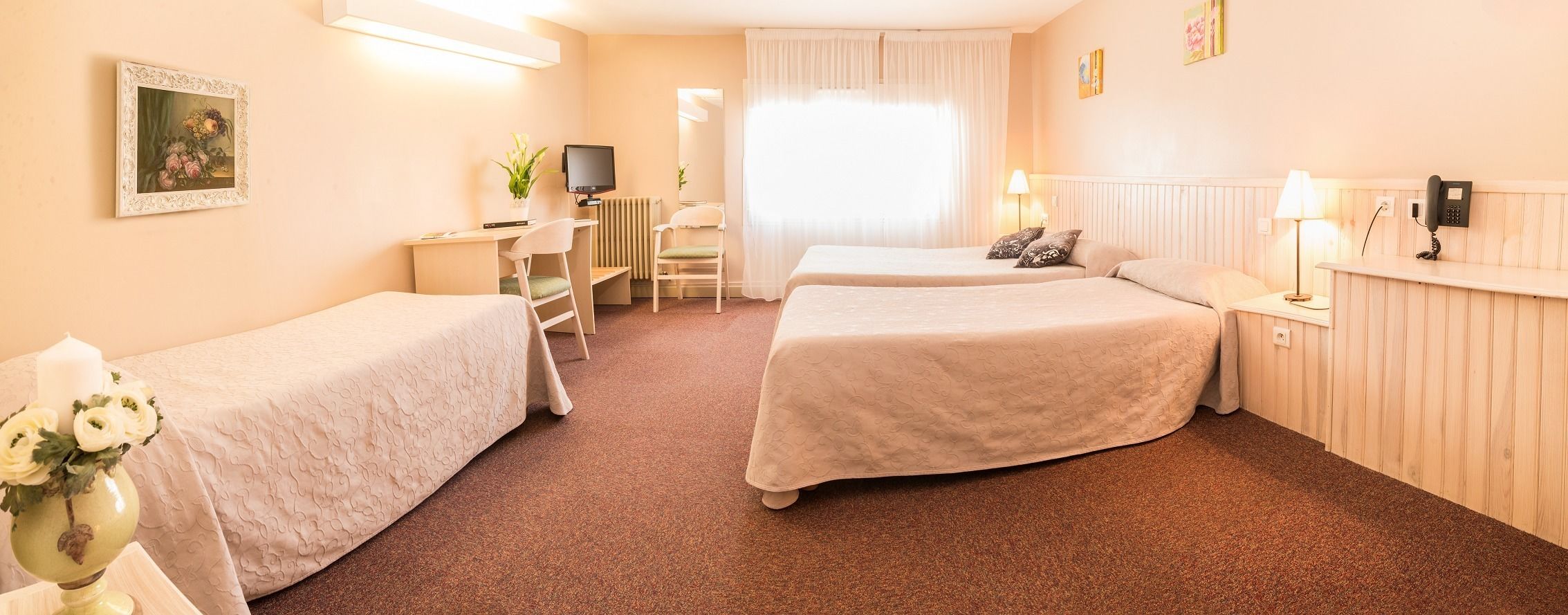 A hotel room with two single beds, a desk with a chair, a TV, a radiator, and a phone on the wall.