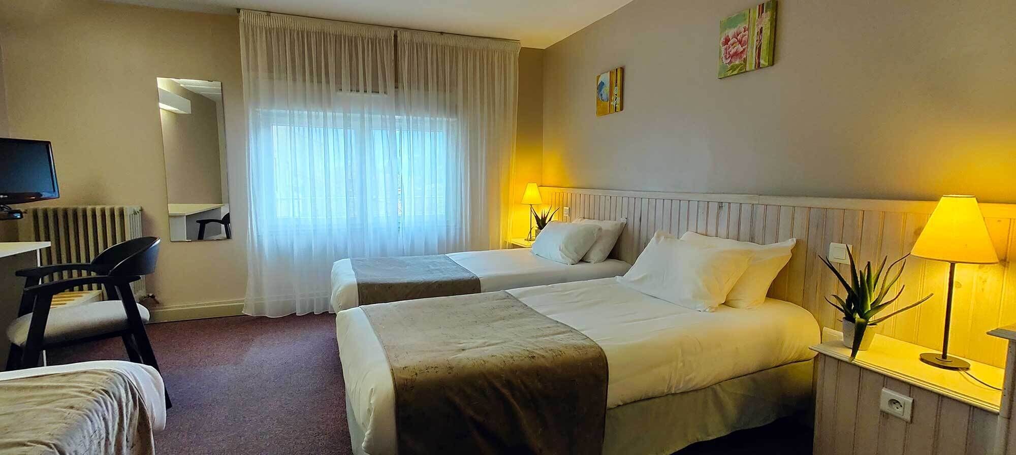 A hotel room with two beds, a desk, a chair, a TV, and a window with curtains.