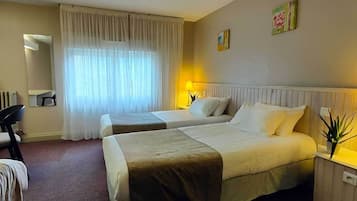 A hotel room with two beds, a desk, a chair, a TV, and a window with curtains.