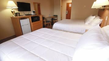 A hotel room with two beds, a desk with a lamp, a television, and a small refrigerator.