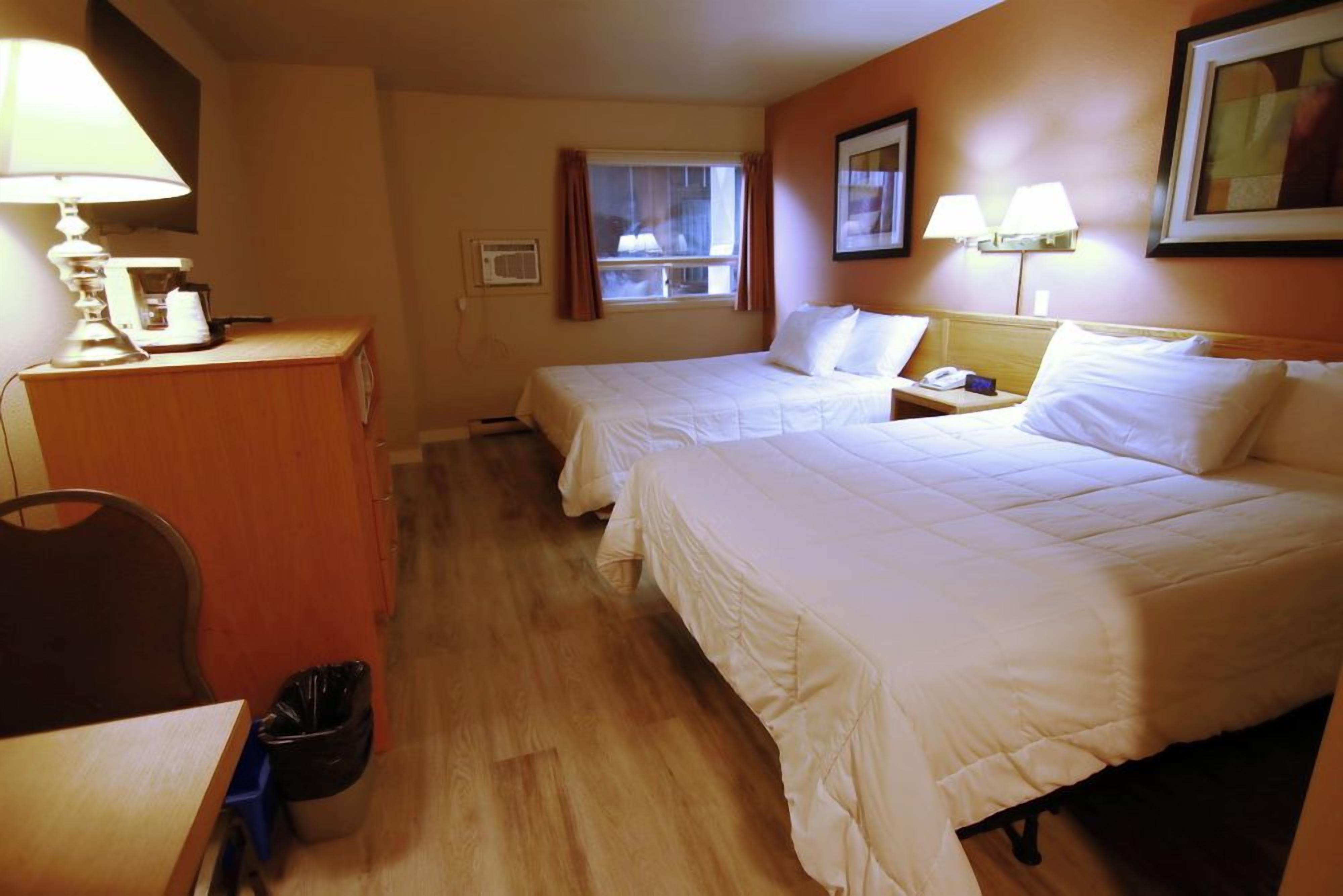 A hotel room with two beds, a desk, a chair, a trash bin, and a window with curtains.