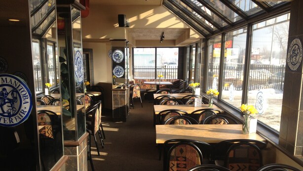 L’intérieur d’un restaurant, avec des tables et des chaises, un mur en verre donnant sur l’extérieur et un logo sur le mur.