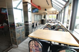 Un restaurante con varias mesas y sillas, un salpicadero de azulejos y amplias ventanas.