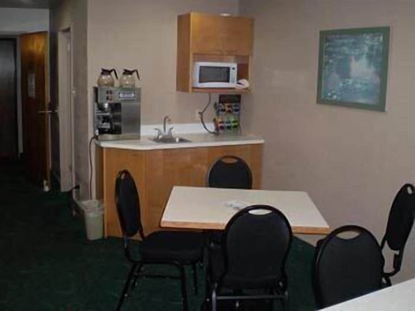 A compact hotel room with a kitchenette, a dining table with four chairs, and a framed picture on the wall.