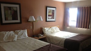 Une chambre d’hôtel avec deux lits, une table de chevet avec une lampe et des œuvres d’art encadrées accrochées aux murs.