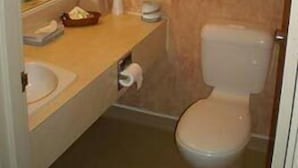 Une petite salle de bain avec des toilettes, un lavabo et un miroir. Une serviette est accrochée au mur et une poubelle est posée sur le sol.