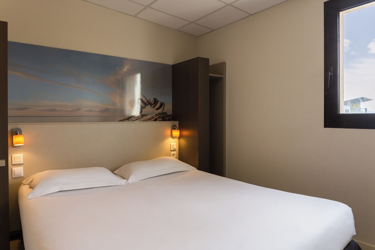 Une chambre d’hôtel avec un lit, un tableau au mur et une fenêtre.