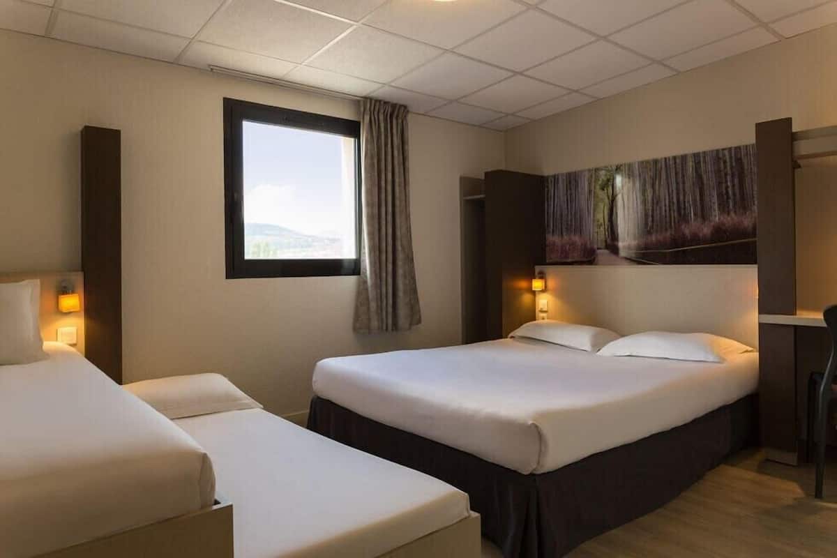 Een hotelkamer met twee bedden, een groot raam, een schilderij aan de muur en een bureau met een stoel.