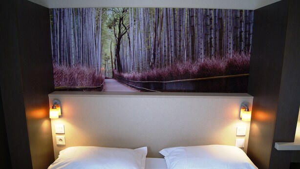 A hotel room with a bed, two wall-mounted lights, and a large forest-themed wall hanging.