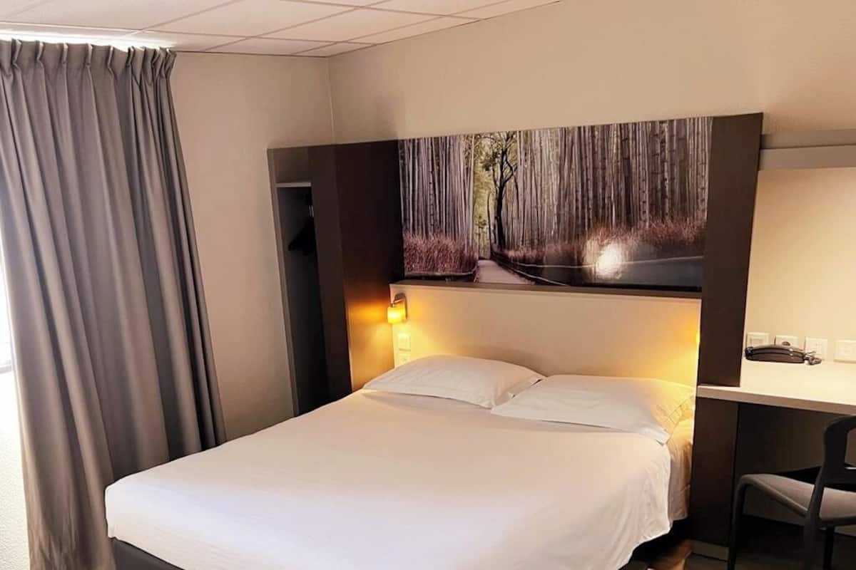 Een hotelkamer met een bed, een bureau en een schilderij aan de muur.