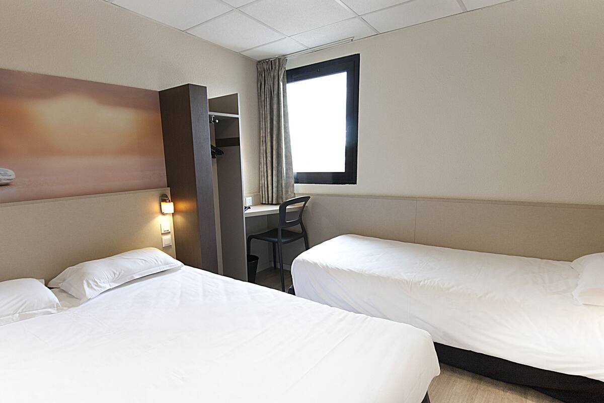 Een hotelkamer met twee bedden, een bureau, een stoel en een raam met gordijnen.