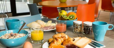 Une table mise pour le petit-déjeuner avec un bol de céréales, des croissants, des toasts et du jus de fruits.