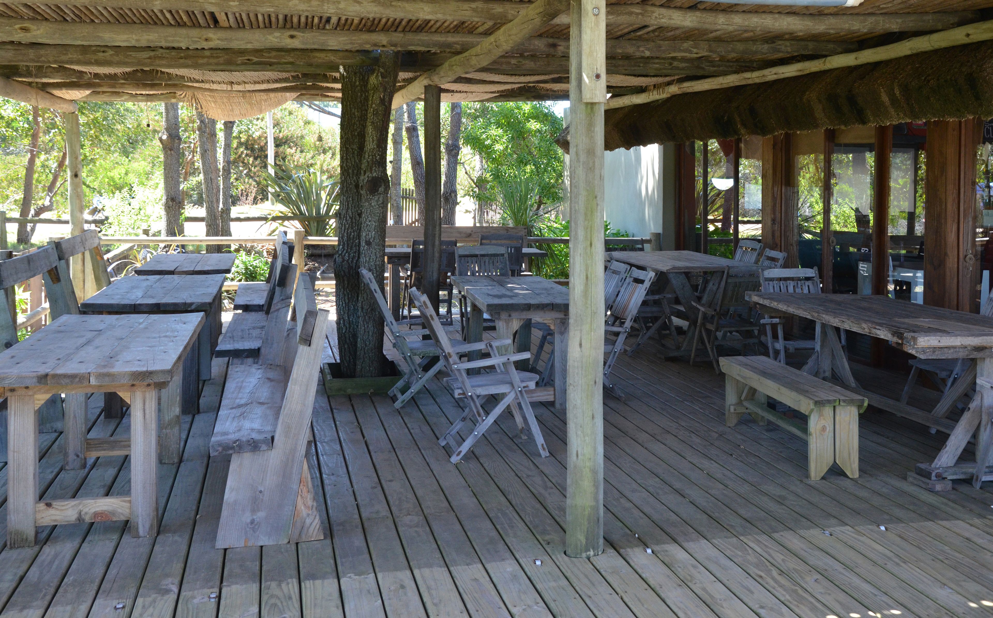 An outdoor wooden deck with picnic tables and benches, surrounded by trees.