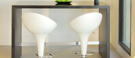 Two white bar stools with chrome bases and a black table with a green bowl on top.