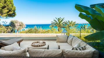 A sunlit outdoor seating area with a view of the sea, featuring wicker furniture and a small table with a tray.