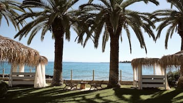 Un lounge frente a la playa con palmeras, una estructura de techo de paja y vista al mar.