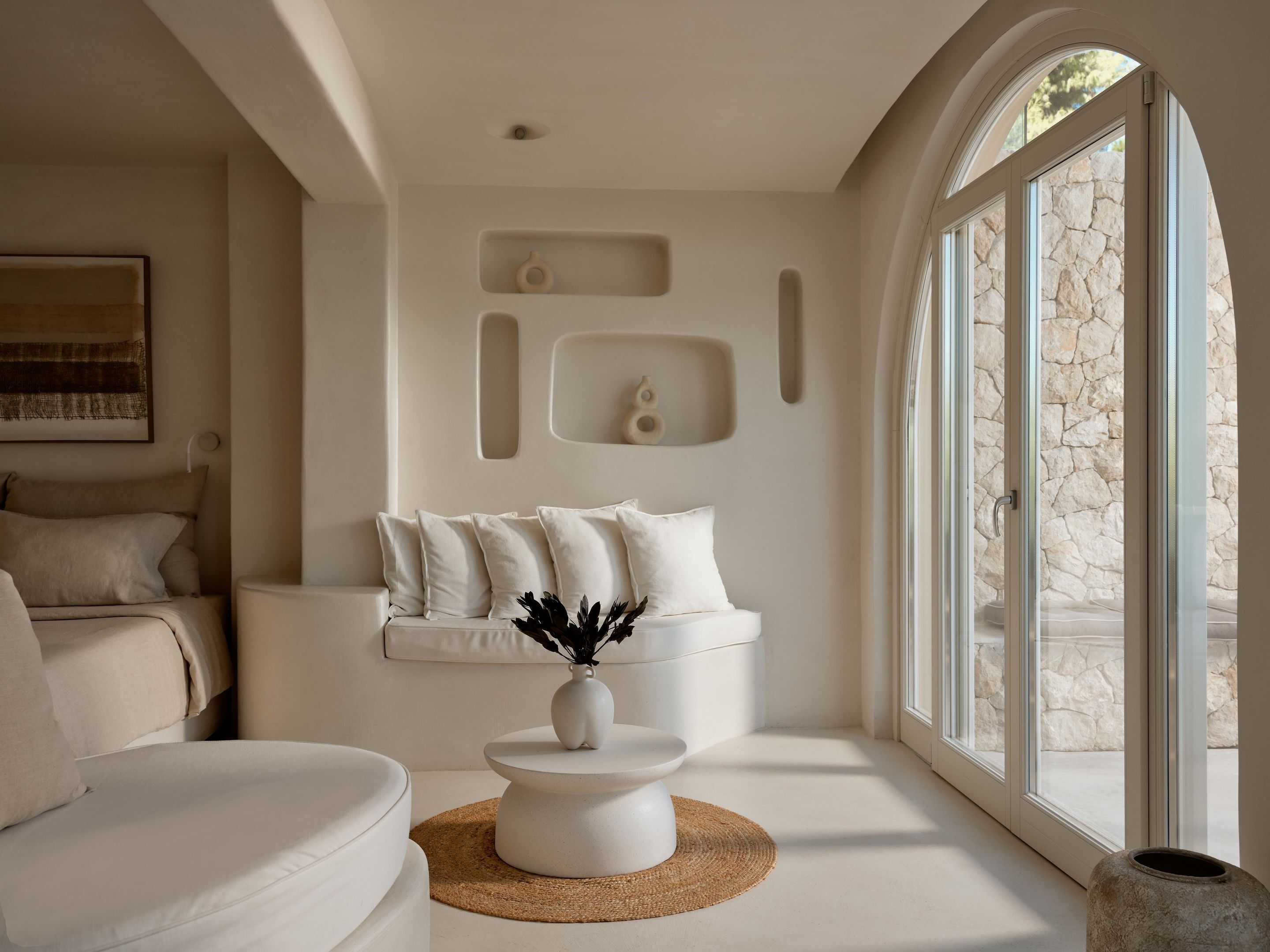 A modern living room with a white sofa, a coffee table, and a stone wall.