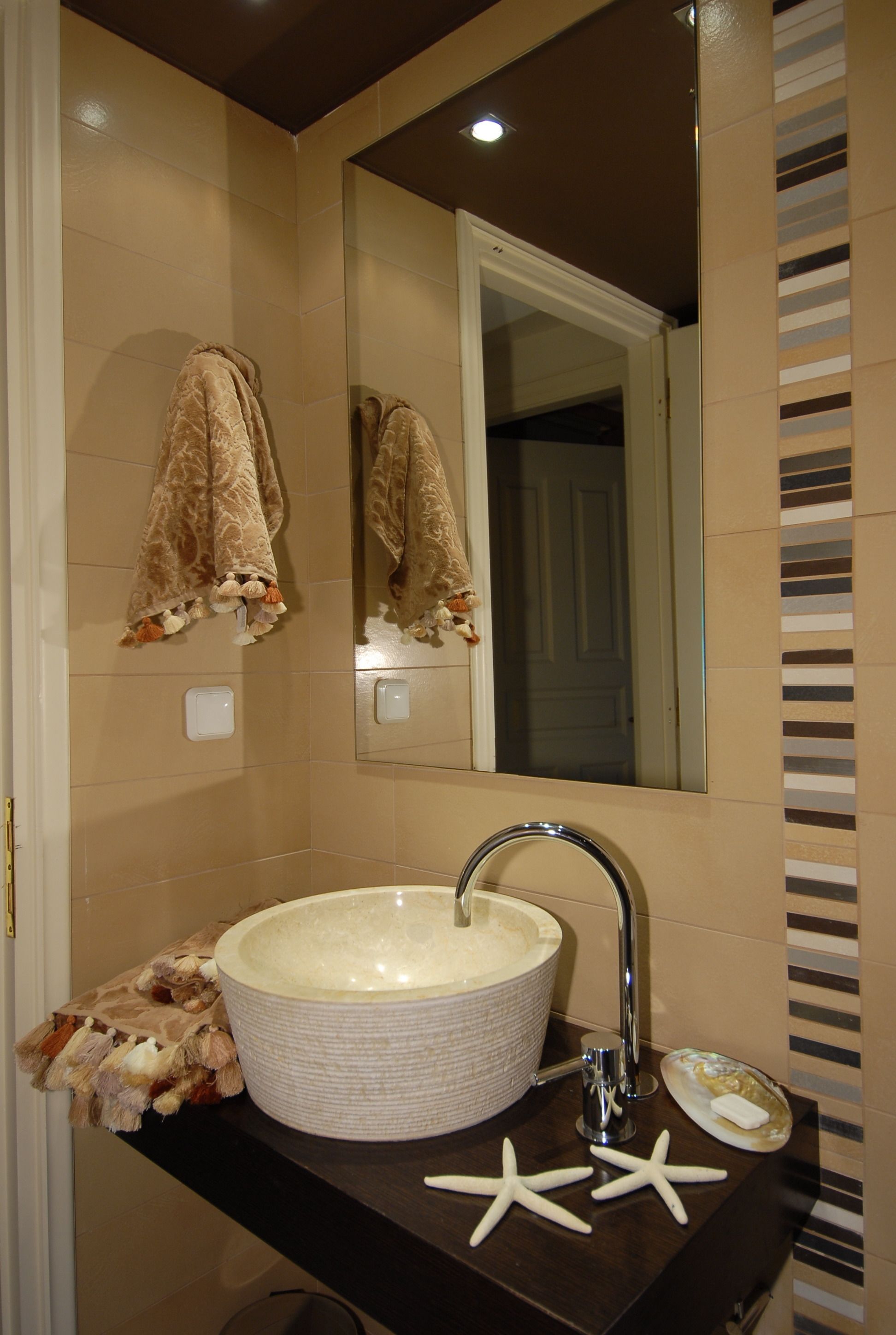 A bathroom with a large round sink, a mirror, and a towel rack with a patterned towel.