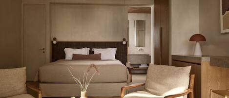 A bedroom with a bed, two chairs, a small table, a nightstand, a ceiling fan, a mirror, and a lamp.