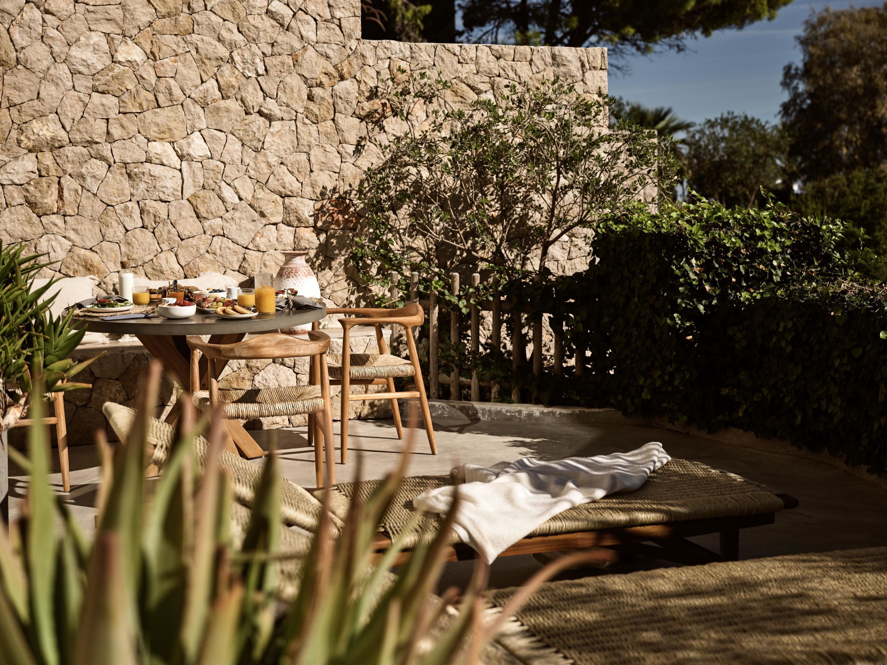 An outdoor dining area with stone walls, wicker furniture, and a variety of dishes and drinks on the table.