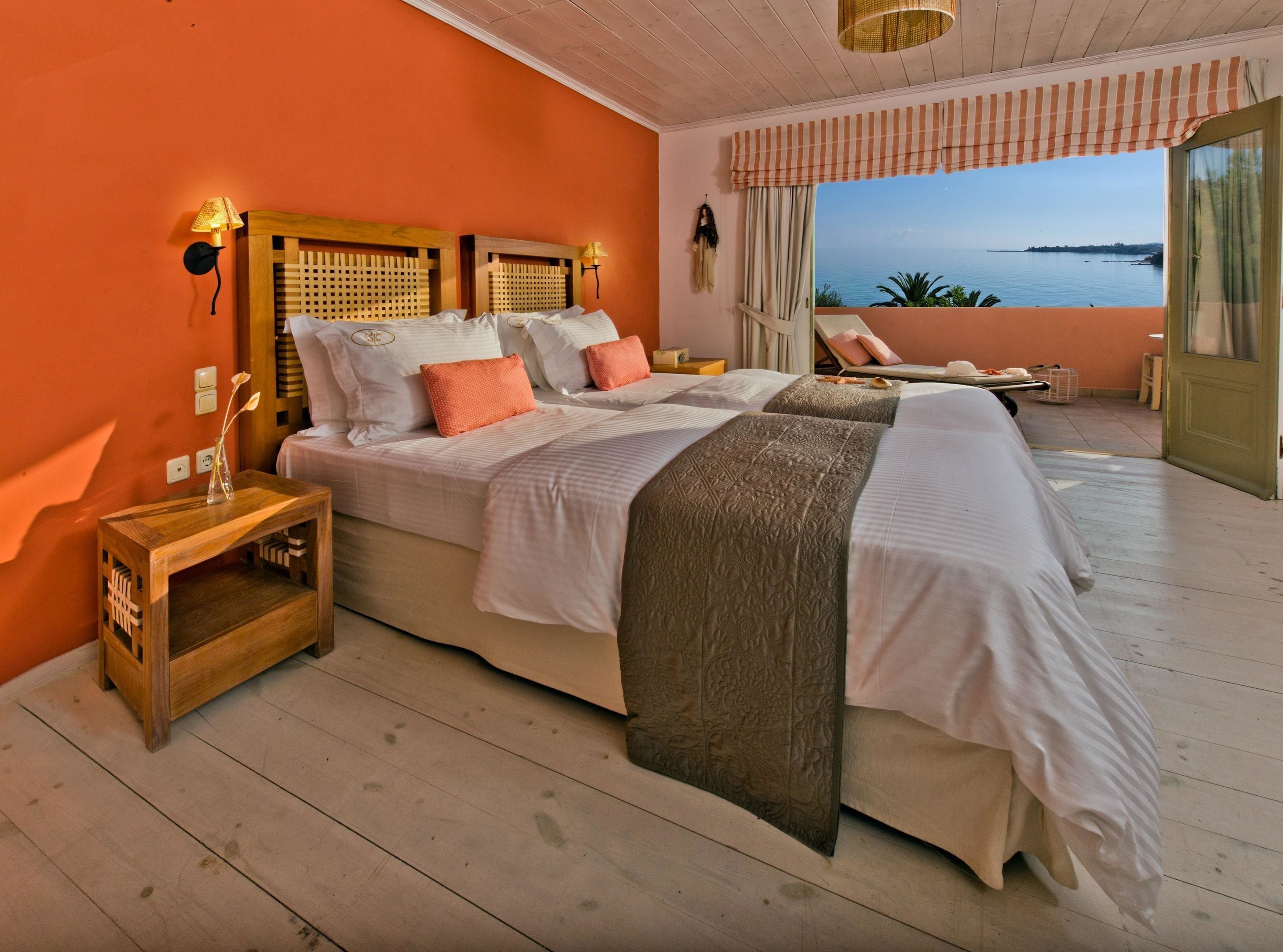 Ein Schlafzimmer mit zwei Betten, einem Nachttisch aus Holz, Meerblick und einem Balkon mit einem Stuhl.