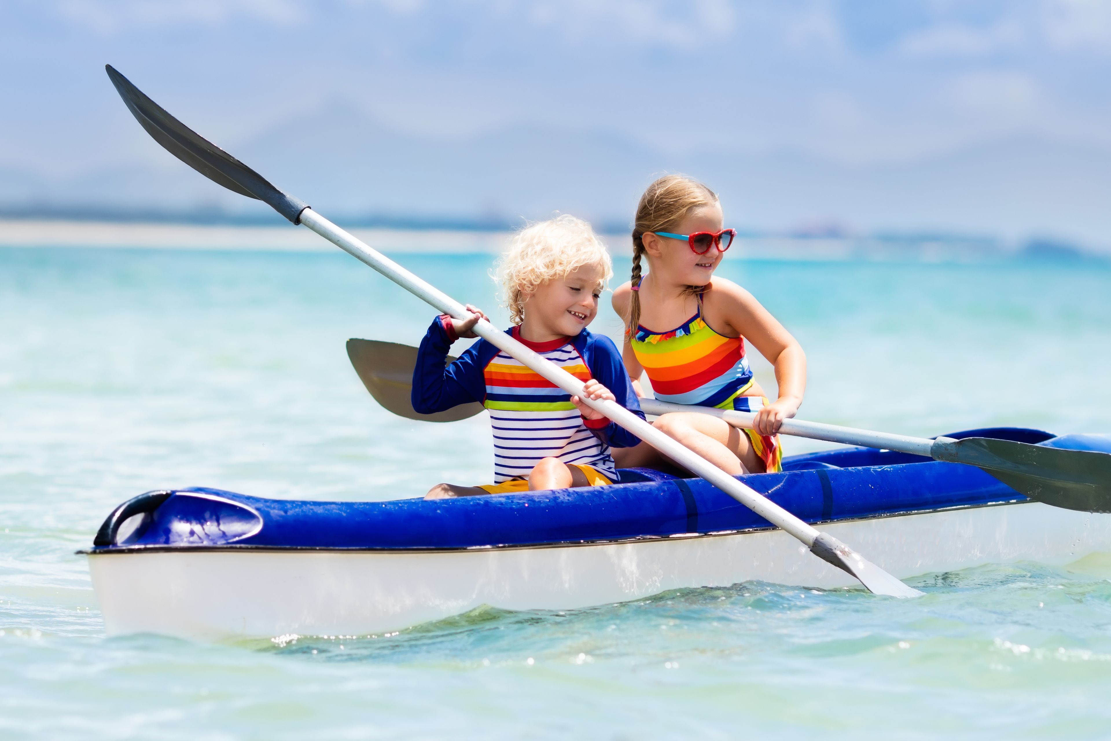 Dos niños en un pequeño bote azul y blanco sobre aguas tranquilas.