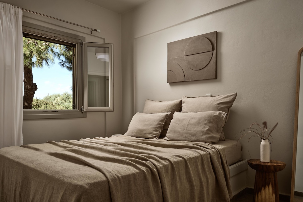 A bedroom with a bed, a window with curtains, a bedside table, and a wall-mounted artwork.