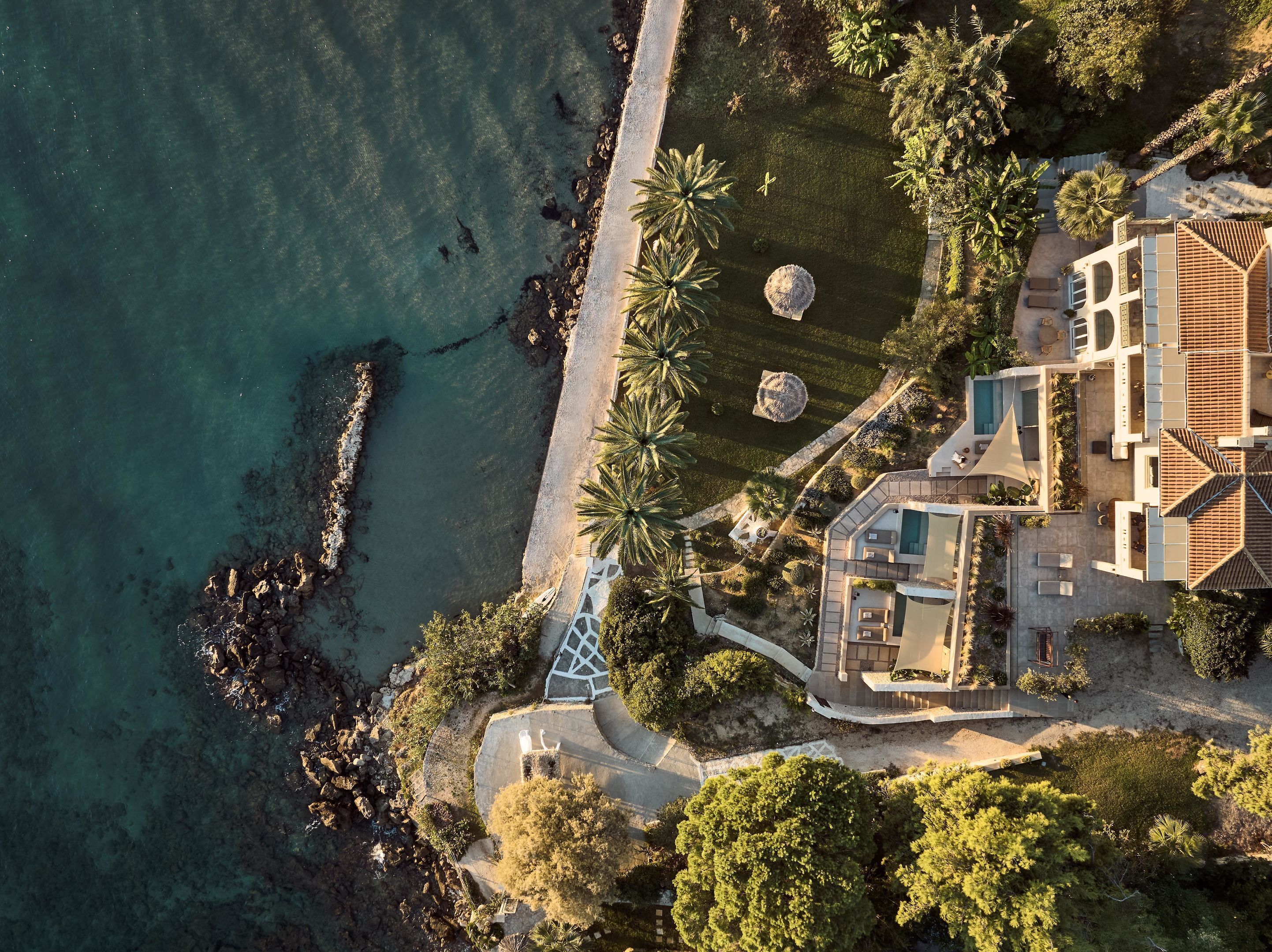 Vista aérea de una propiedad costera con piscina, zona de patio y camino de acceso a la playa.