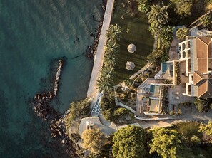 An aerial view of a coastal property with a swimming pool, a patio area, and a beach access path.