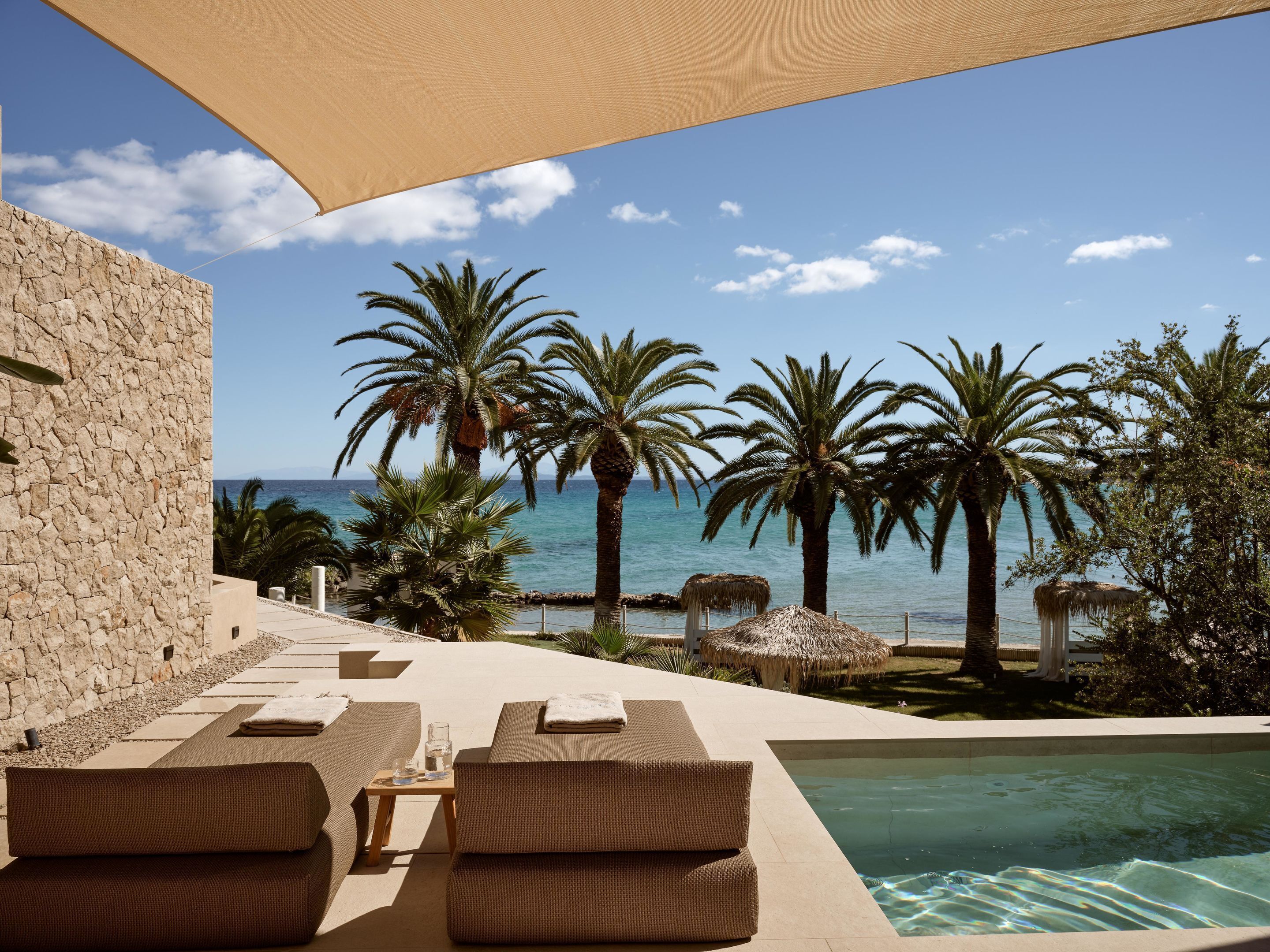 A poolside area with lounge chairs, a pool, and a view of the sea and palm trees.