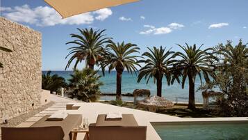 A poolside area with lounge chairs, a pool, and a view of the sea and palm trees.