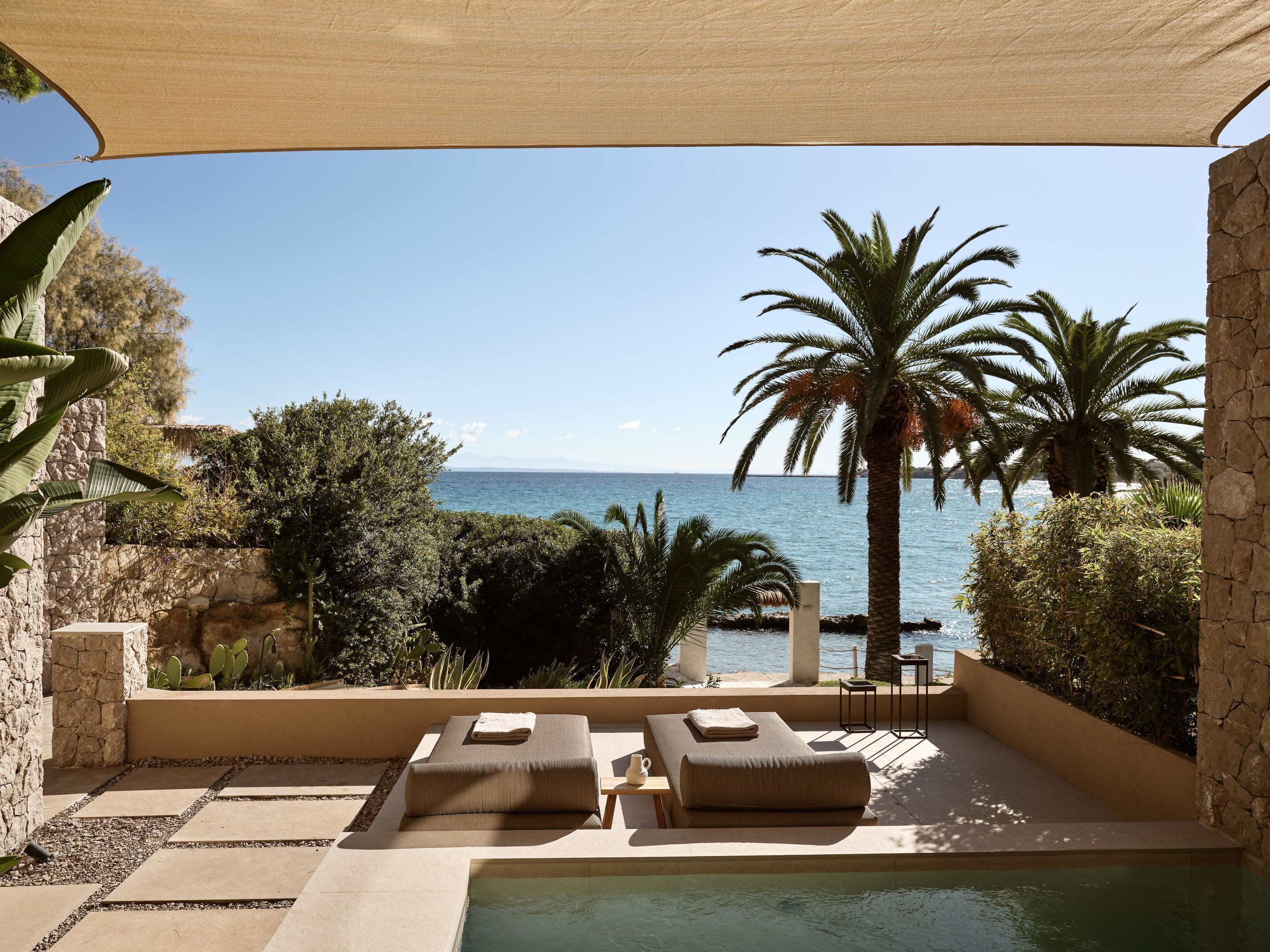 Área à beira da piscina com espreguiçadeiras, vista para o mar e plantas tropicais.