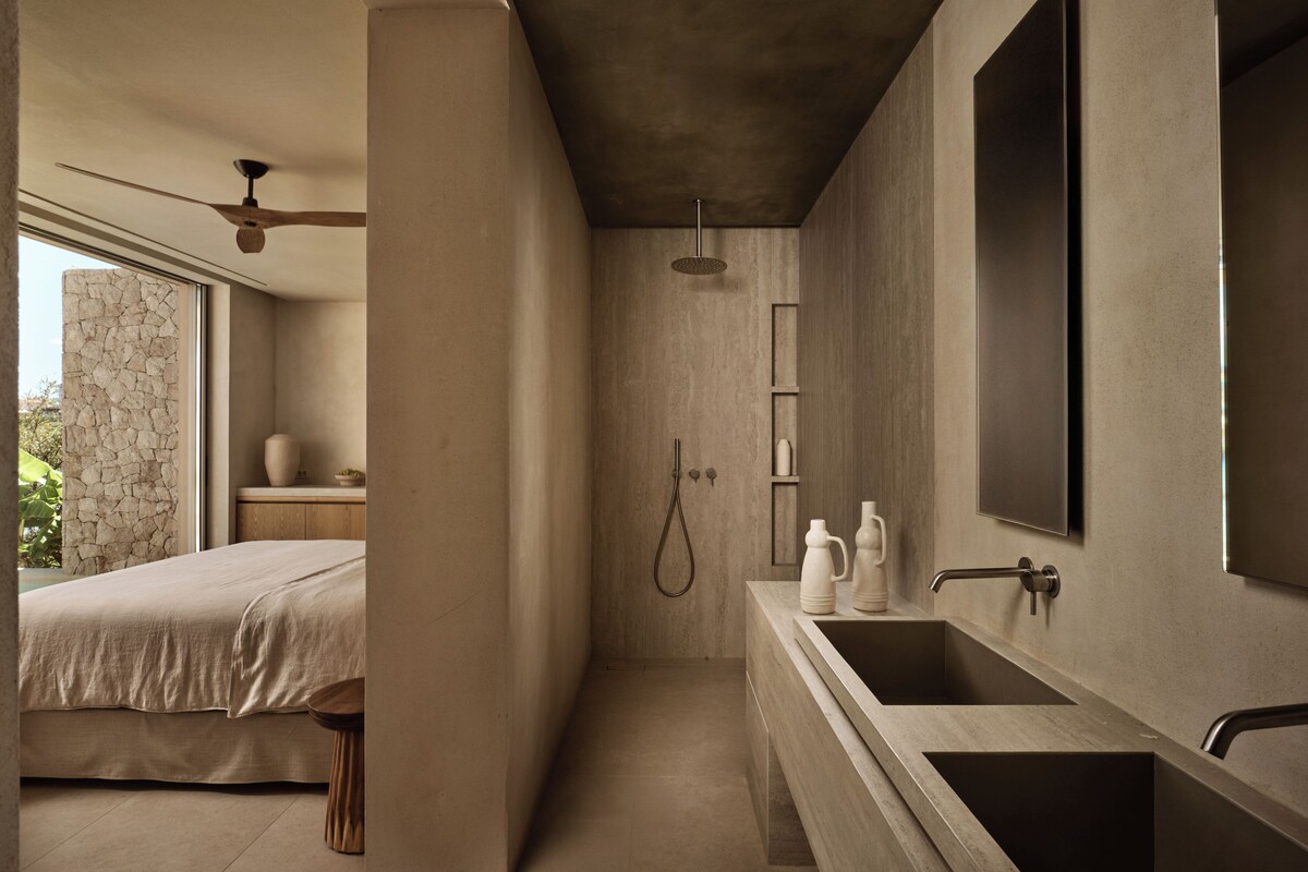 A modern bathroom with a large sink, a shower, and a bed with a view of the outdoors.