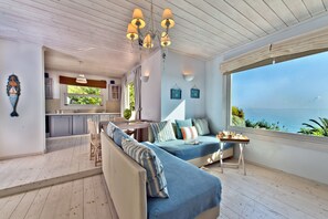 Un interior moderno con piso de madera, un sofá con cojines a rayas, un comedor y vistas al mar.