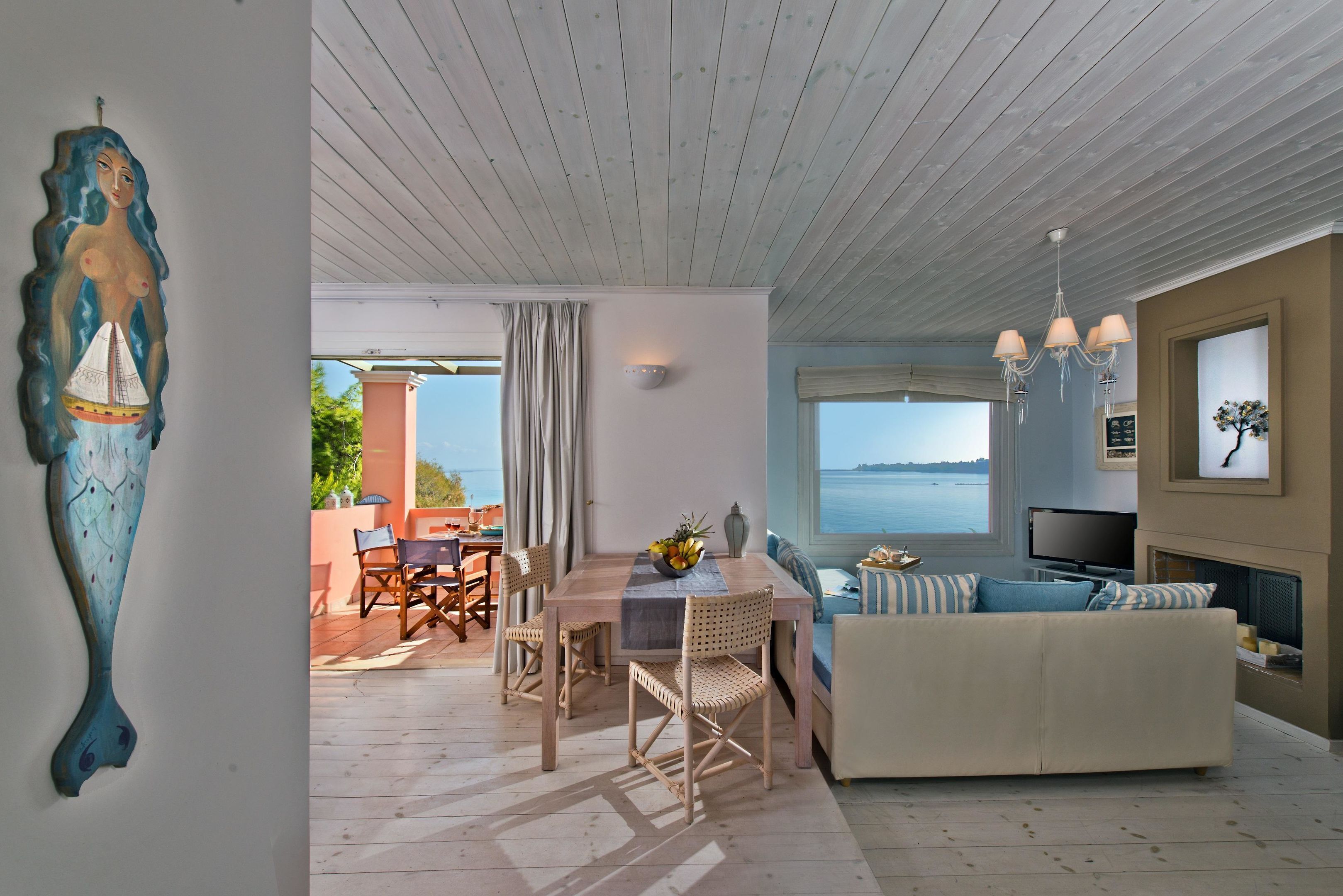 Ein modernes Wohnzimmer mit Holzboden, einer Couch, einem Esstisch mit Stühlen und Meerblick.