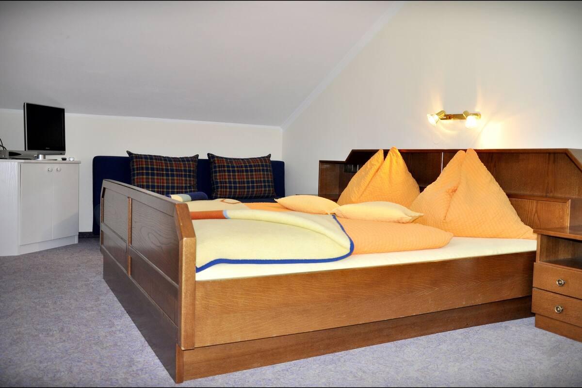 Ein Schlafzimmer mit einem hölzernen Bett, einem Schreibtisch mit Computer und einem Fernseher auf einem Schrank.