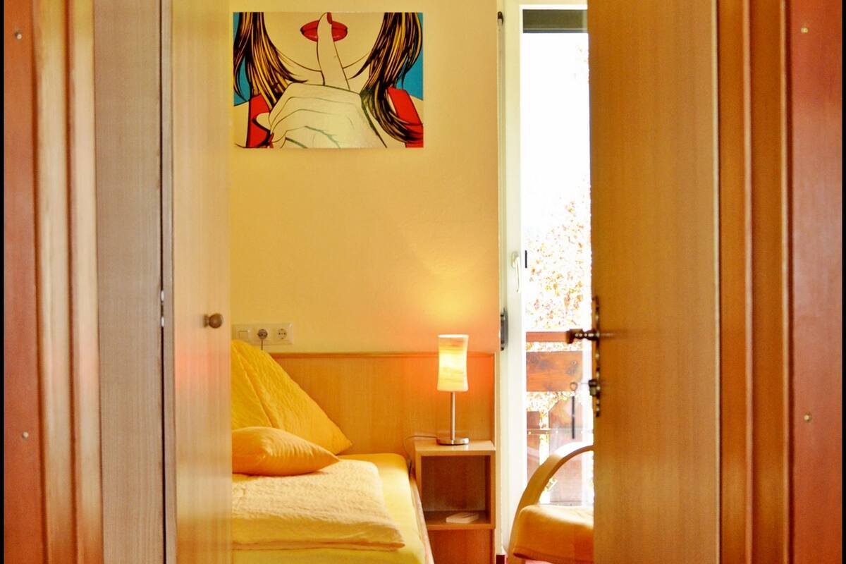 Ein Zimmer mit einem Bett, einem Nachttisch, einer Lampe und einem Sessel.