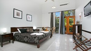 A well-lit bedroom with a large bed, bedside tables, a desk, and a chair. There is a TV mounted on the wall and a window with curtains. - Daintree Wild Zoo & B&B (Lower Daintree)