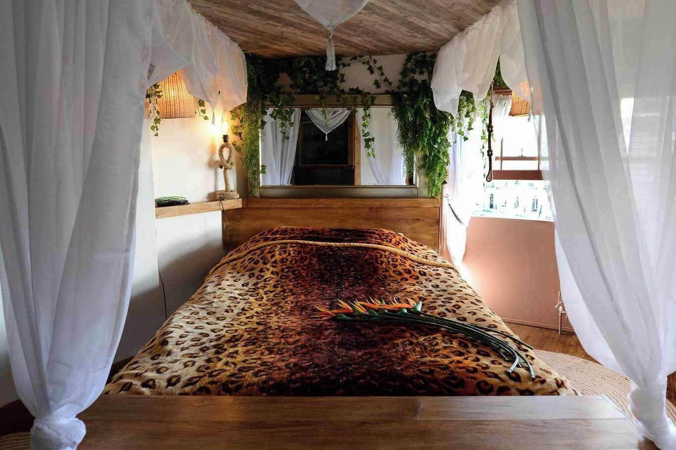 Una cama con una colcha de estampado de leopardo, cortinas blancas y una planta colgante.