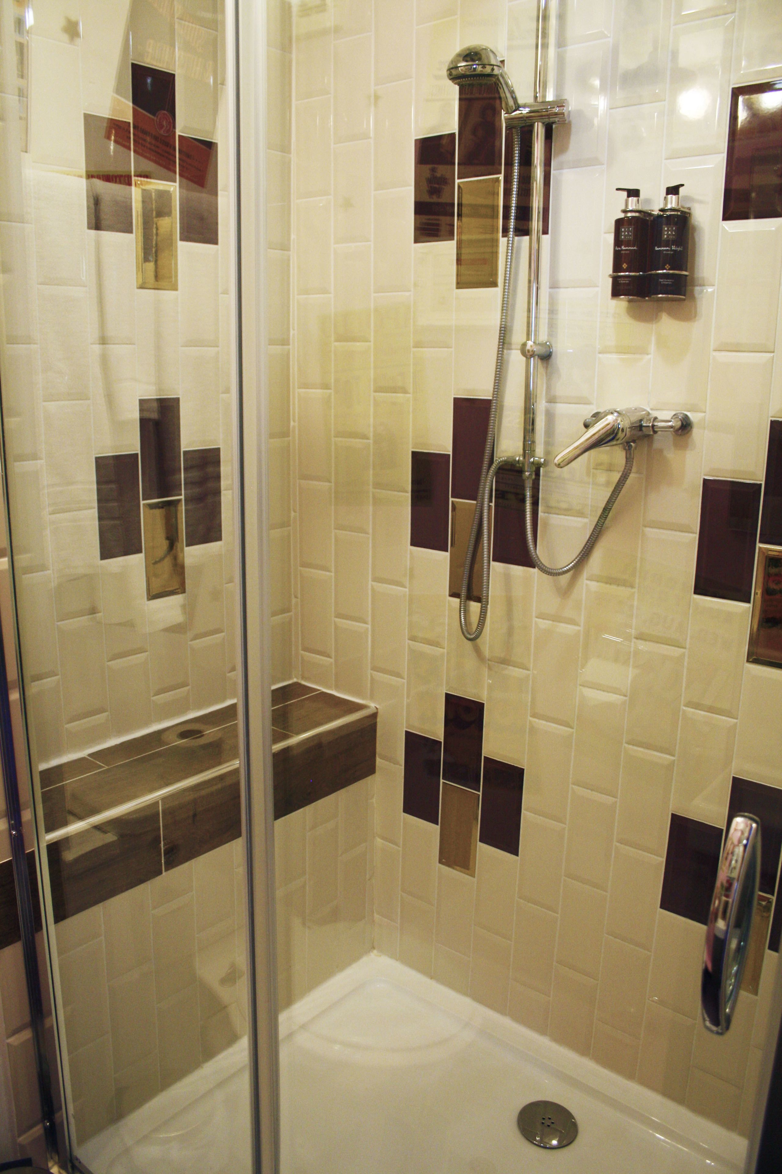 Une douche fermée par des parois en verre, dotée d’un pommeau de douche à main et d’un robinet fixé au mur.