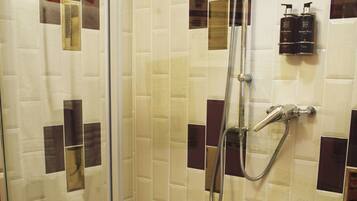 Une douche fermée par des parois en verre, dotée d’un pommeau de douche à main et d’un robinet fixé au mur.