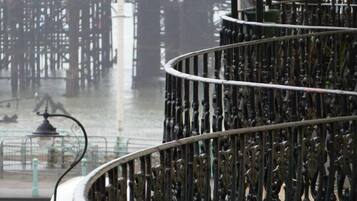 A spiral staircase with ornate metal railings, leading to a balcony overlooking a waterfront with industrial structures.