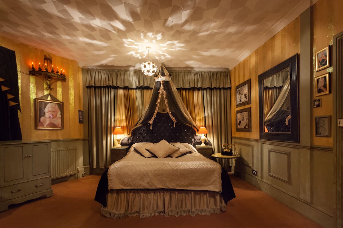 Ein Schlafzimmer mit Himmelbett, einer Chandelierleuchtre und gerahmten Bildern an den Wänden.